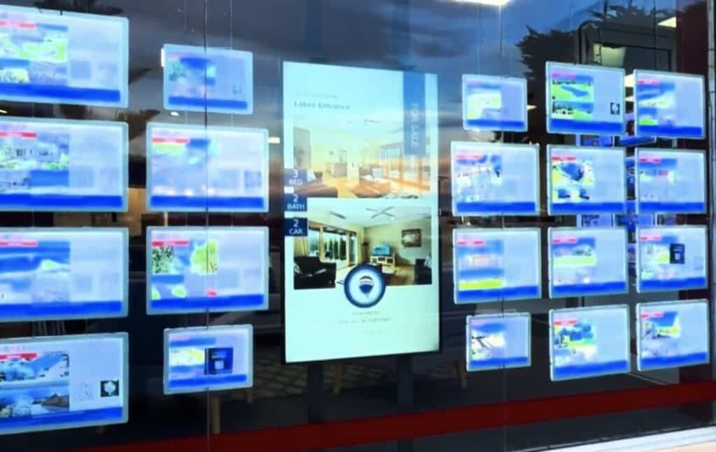 RE/MAX Genesis shop front window with listing screens and a property story video playing